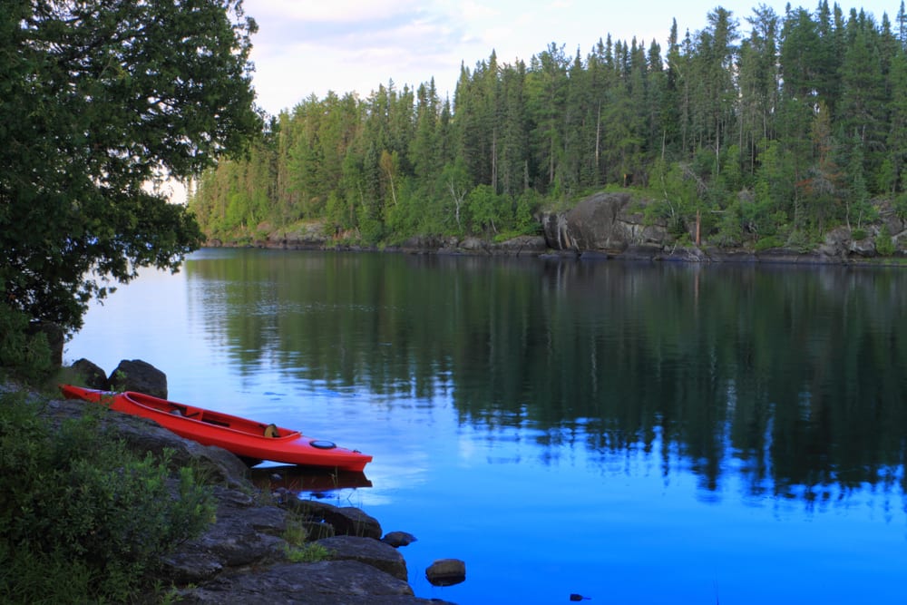 Red kayak sitting on shore of calm lake.